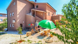 A multi-story building with a patio area featuring outdoor furniture, a grill, and a green umbrella. - Holiday apartment with garden for shared use and children's playground (Ližnjan)