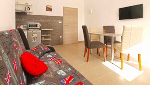 A compact living space with a sofa, a dining table, and a TV mounted on the wall. - Holiday apartment with garden for shared use and children's playground (Ližnjan)