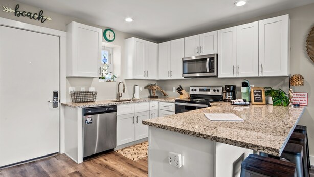 A modern kitchen with white cabinets, a granite countertop, stainless steel appliances, and a clock on the wall. - Remodeled 3BR Condo: Private Beach Access, Pool View, & Walking Distance to Town (Port Aransas)