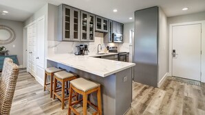 A modern kitchen with a marble island, wooden stools, and stainless steel appliances. - Newly Remodeled 2BR Condo with Private Path to Beach, Pool View, & Close to Town (Port Aransas)