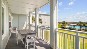 A covered balcony with a table and chairs, overlooking a pool and a grassy area.