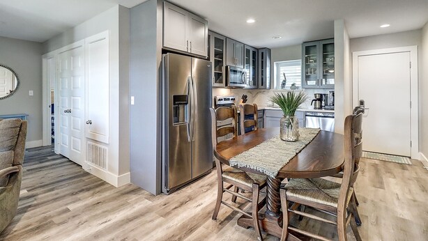 A modern kitchen with stainless steel appliances, wooden dining table, and built-in cabinets.