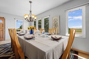 A dining room with a table set for four, a chandelier, and large windows offering a view of the outdoors.