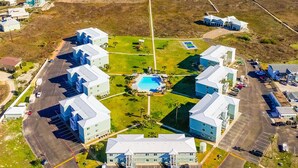 An aerial view of a coastal resort with multiple buildings, a central pool, and a beach in the background. - 3BR Condo w/ Pool View, Private Beach Access & Short Walk to Town and the Beach (Port Aransas)