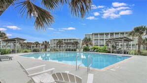A swimming pool with lounge chairs and a building with balconies in the background. - 3BR Condo w/ Pool View, Private Beach Access & Short Walk to Town and the Beach (Port Aransas)