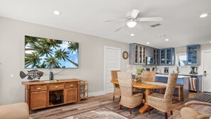 A modern kitchen with blue cabinets, a dining area with wicker chairs, and a ceiling fan. - 3BR Condo w/ Pool View, Private Beach Access & Short Walk to Town and the Beach (Port Aransas)