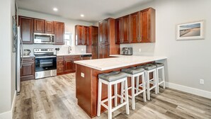 A modern kitchen with wooden cabinets, stainless steel appliances, and a central island with bar stools. - Luxury Gulf-View Penthouse – Top Floor 3BR Condo (Port Aransas)