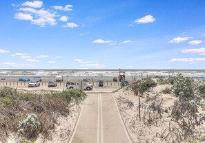 Stroll along the beachside path to the sandy beach area, bordered by lush vegetation and offering access to the ocean.