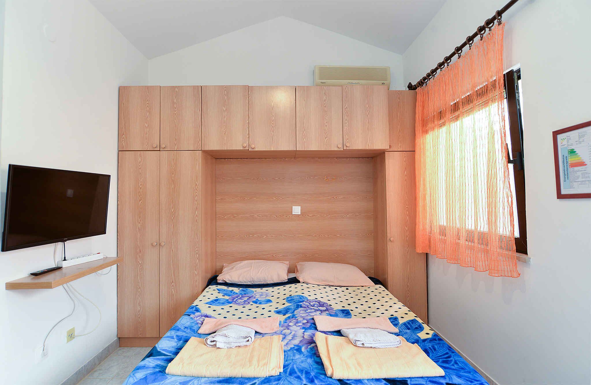 A bedroom with a bed, a TV, and a window with curtains.