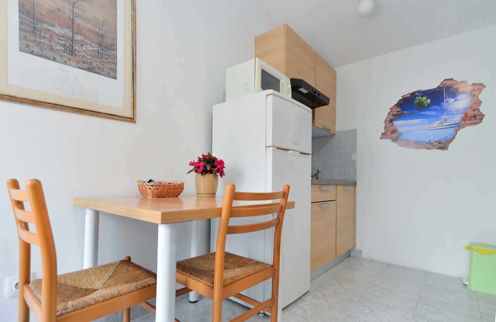 Ett litet kök med ett vitt kylskåp, träskåp och ett matbord med två stolar.