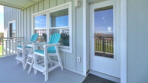 A porch with white railings, a set of turquoise Adirondack chairs, and a door with a view of a fenced yard. - Experience Paradise in this Recently Remodeled 3BR/2BA (Port Aransas)