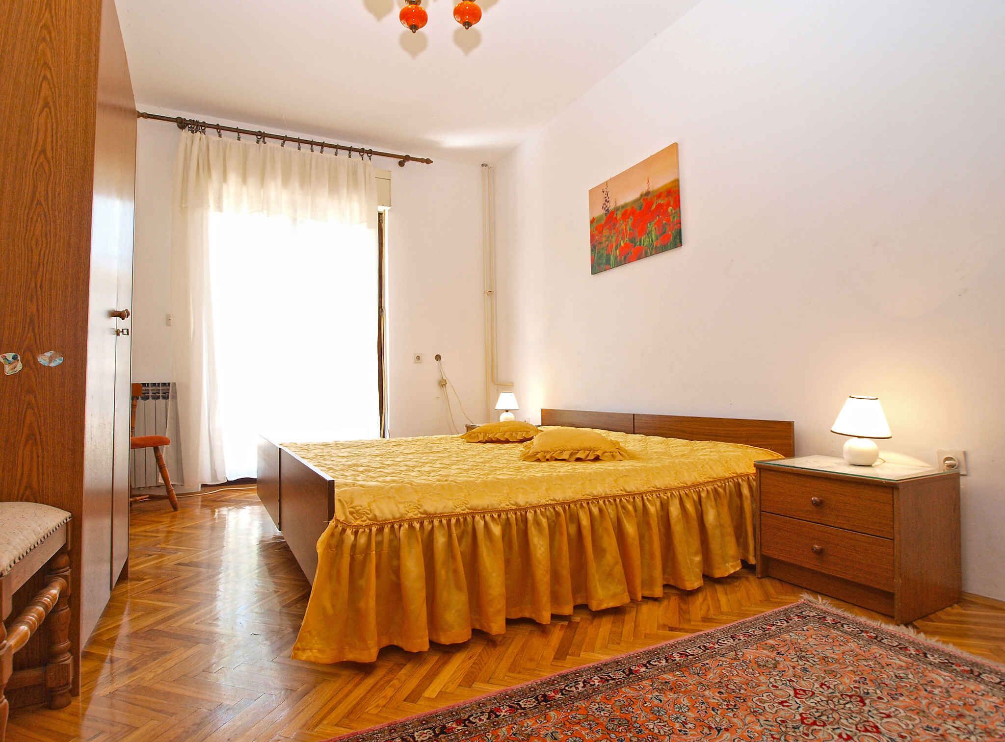 A bedroom with a wooden bed, a nightstand with a lamp, a patterned rug, and a painting on the wall.