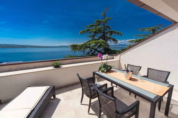 A balcony with a table and chairs, overlooking a body of water and a tree.