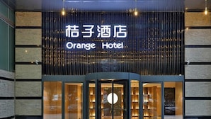 Exterior do Hotel Orange com design moderno, apresentando uma entrada por porta giratória e uma placa em chinês e inglês.