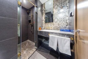 Un baño moderno con ducha envuelta en vidrio, tocador de mármol y un salpicadero con diseño.