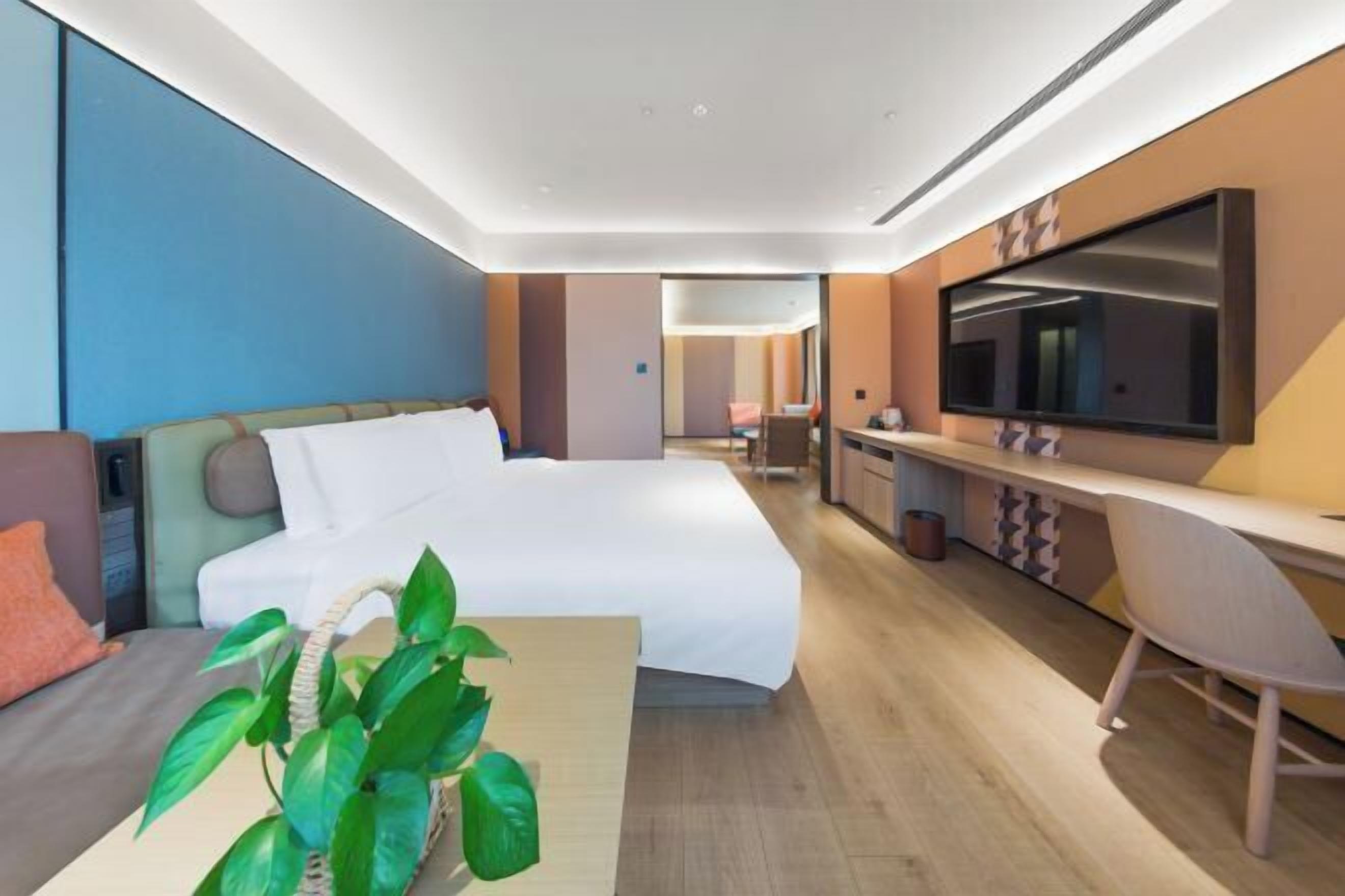Une chambre d’hôtel moderne équipée d’un grand lit, d’un bureau, d’une télévision à écran plat et d’une plante en pot.