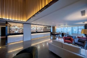 A modern hotel lobby with a reception desk, seating area, and large windows.