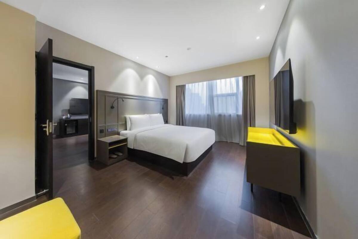 Une chambre d’hôtel moderne équipée d’un lit, d’une table de chevet, d’une télévision et d’un banc jaune.