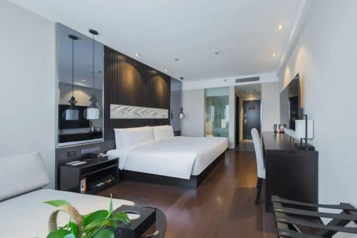 A modern hotel room with a large bed, a desk, and a seating area.