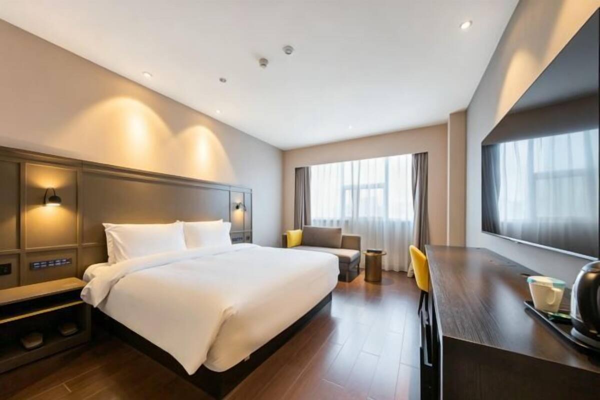 Une chambre d’hôtel moderne, dotée d’un grand lit, d’un bureau, d’une chaise, d’une télévision et d’une fenêtre avec des rideaux.
