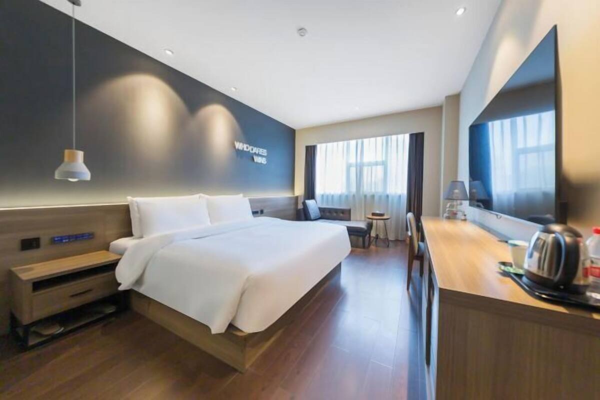 Une chambre d’hôtel moderne avec un grand lit, un bureau avec une bouilloire, une petite table et un téléviseur.