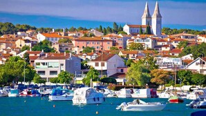 Un pueblo costero con un puerto deportivo lleno de barcos, edificios históricos y una iglesia destacada con dos torres.