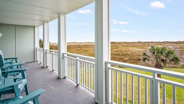 A covered porch with white railings, a view of a grassy landscape, and a palm tree.