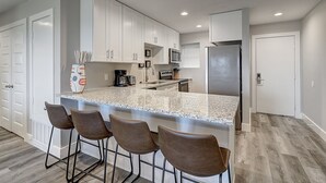 A modern kitchen with white cabinets, a granite countertop, and four bar stools.