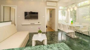 A modern living room with a sofa, a coffee table with a plant, a TV mounted on the wall, and a dining area with chairs and a table. - Holiday apartment with air conditioning (Crikvenica)