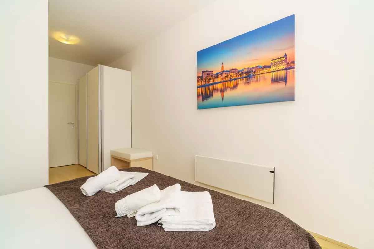 A hotel room with a bed, towels, a painting of a cityscape, and a radiator.