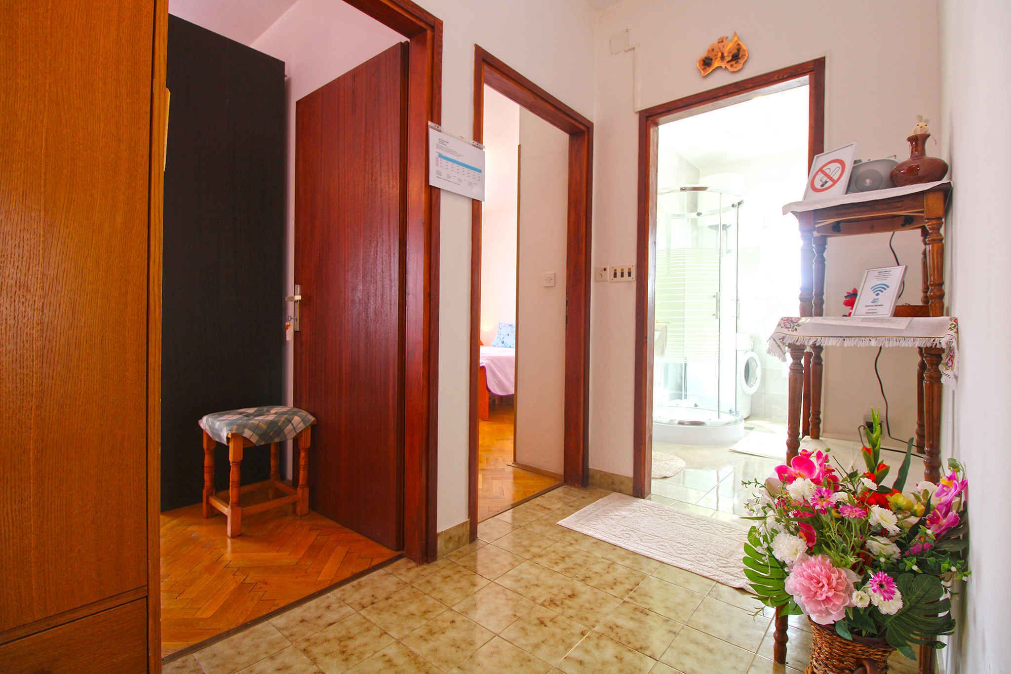 Um corredor com porta de madeira, um banquinho pequeno, uma placa na parede e um cesto de flores.