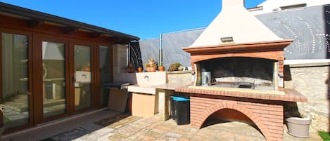 An outdoor kitchen with a brick oven, a countertop, and a trash can.