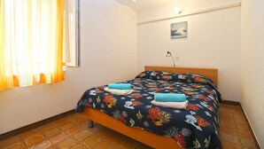 A bedroom with a bed, curtains, a wall-mounted picture, and a tiled floor.
