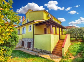 Una casa de dues plantes amb fonaments de pedra, façana groga i teulat vermell.