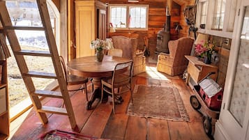 Interno accogliente di una baita rustica con un tavolo da pranzo in legno, sedie, un tappeto decorato e un vecchio stufa.
