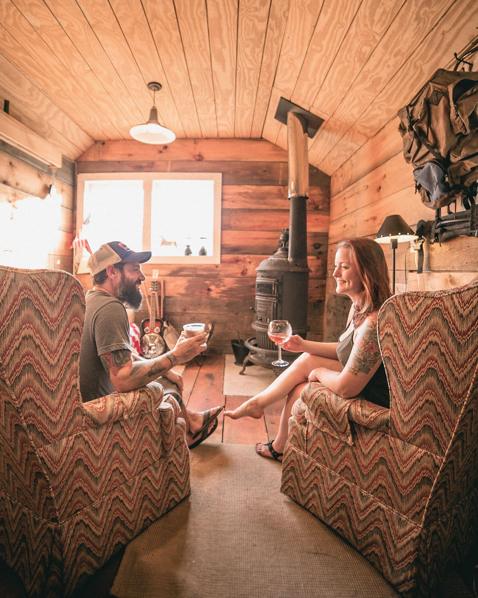 A cozy cabin interior with wooden walls, a fireplace, and two upholstered chairs facing each other.
