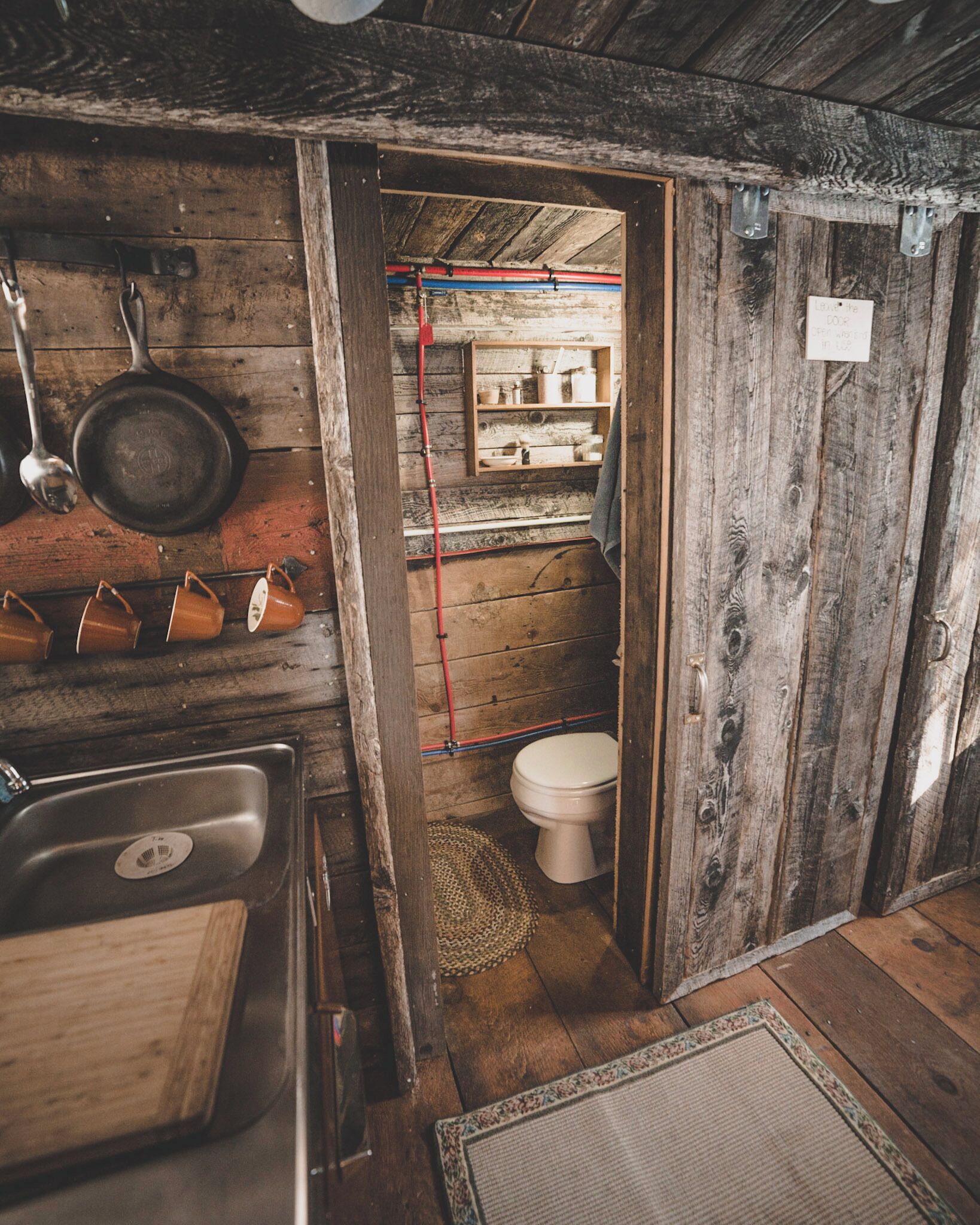 Ein rustikales Holzhaus-Interieur mit Waschbecken aus Holz, einem hängenden Topf und einer Toilette.