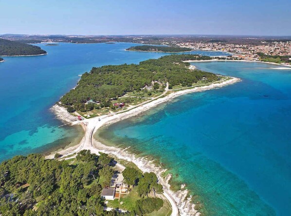 Eine Luftaufnahme einer Küsteninsel mit klarem, blauem Wasser, einem schmalen Sandstrand und dichter Vegetation.