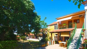 A courtyard with a paved walkway, a dining area with outdoor furniture, and a building with a balcony. - Holiday apartment with garden and barbecue (Pomer)