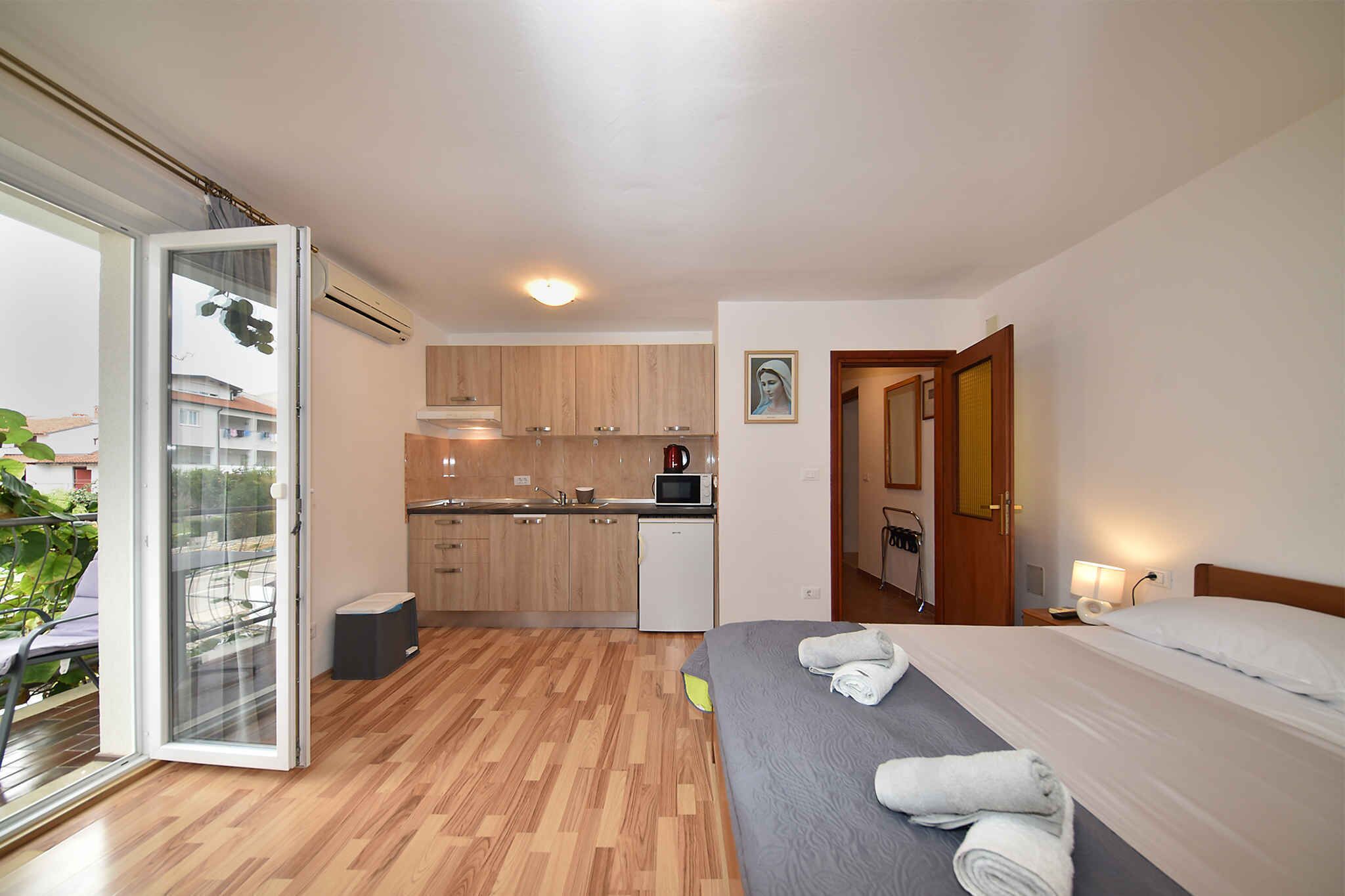 Ein kompaktes Hotelzimmer mit Bett, einer kleinen Küchenzeile, einem Badezimmer und einer Glastür zum Balkon.