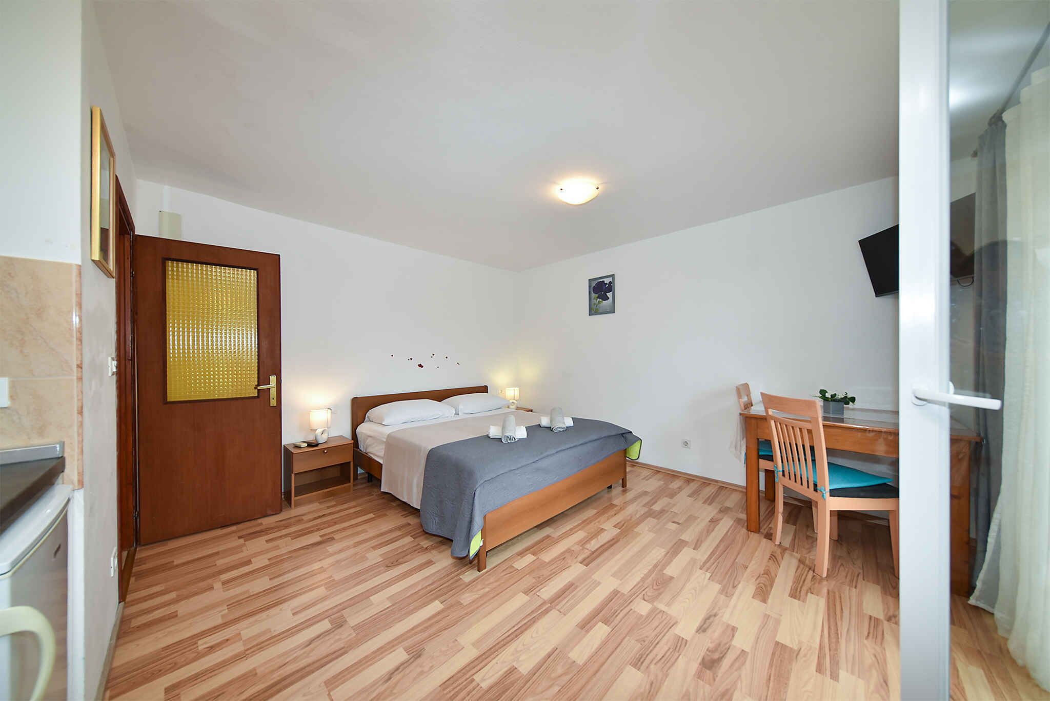 A bedroom with a bed, bedside table, chair, desk, and a small table with a lamp.