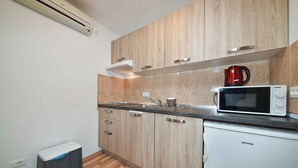 A compact kitchen with wooden cabinets, a stainless steel sink, a microwave, and a red kettle. - Studio with air conditioning (Rovinj)