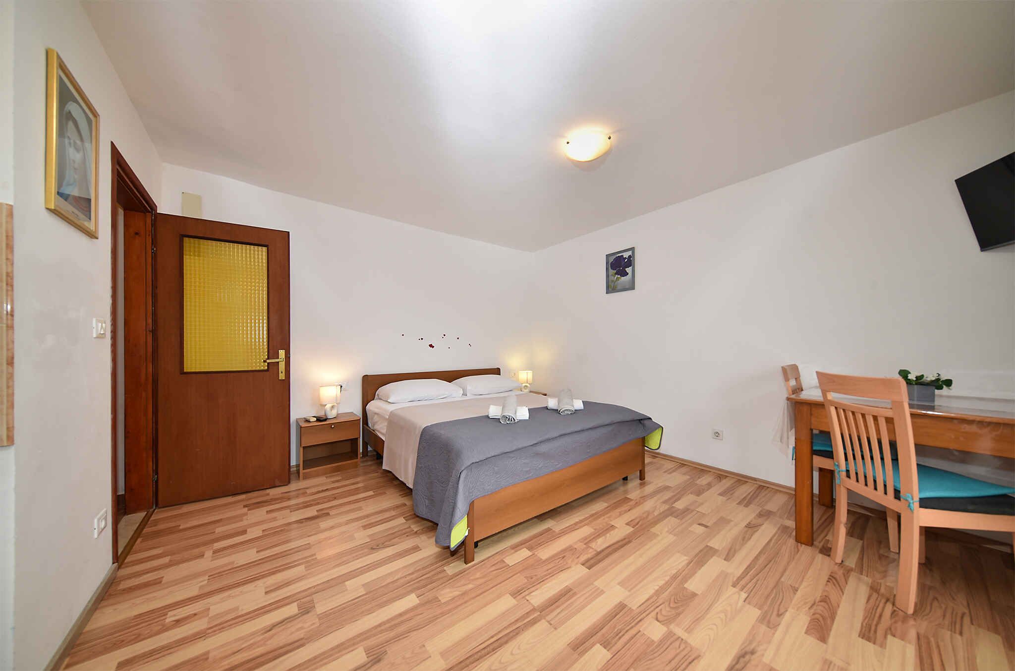 Un dormitorio con una cama de madera, mesitas de noche, un escritorio con silla y un televisor pequeño montado en la pared.
