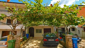 A cobblestone street with parked cars, a tree-lined pathway, and a building with a visible entrance and windows. - Studio with air conditioning (Rovinj)