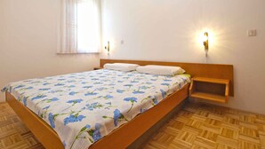 A single bed with a floral bedspread, a bedside table, a nightstand, a window with white curtains, and two wall-mounted lights. - Holiday apartment with pool and barbecue (Novigrad)