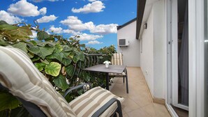 A small outdoor patio with a table and chairs, surrounded by large leafy plants.
