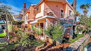 Ein zweistöckiges Haus mit Balkon, umgeben von üppiger Vegetation und Palmen.
