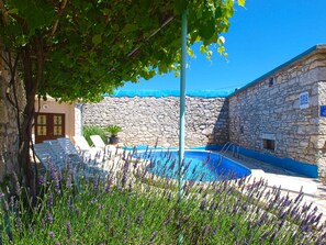 A stone building with a pool, surrounded by lavender plants and a tree.