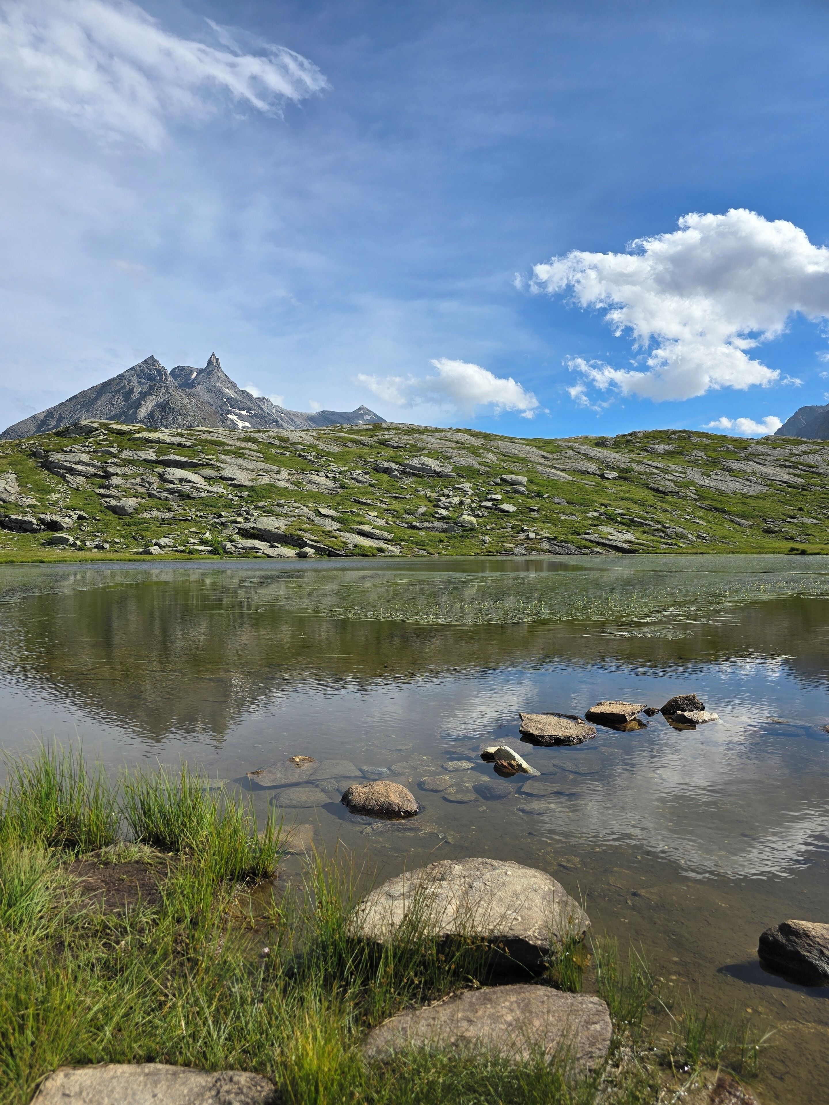 Paisatge de muntanya amb un llac tranquil, envoltat de terreny rocosós i vegetació escassa.