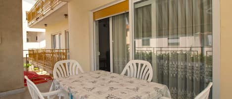 A balcony with a table and chairs, a sliding glass door, and a view of the building's exterior.